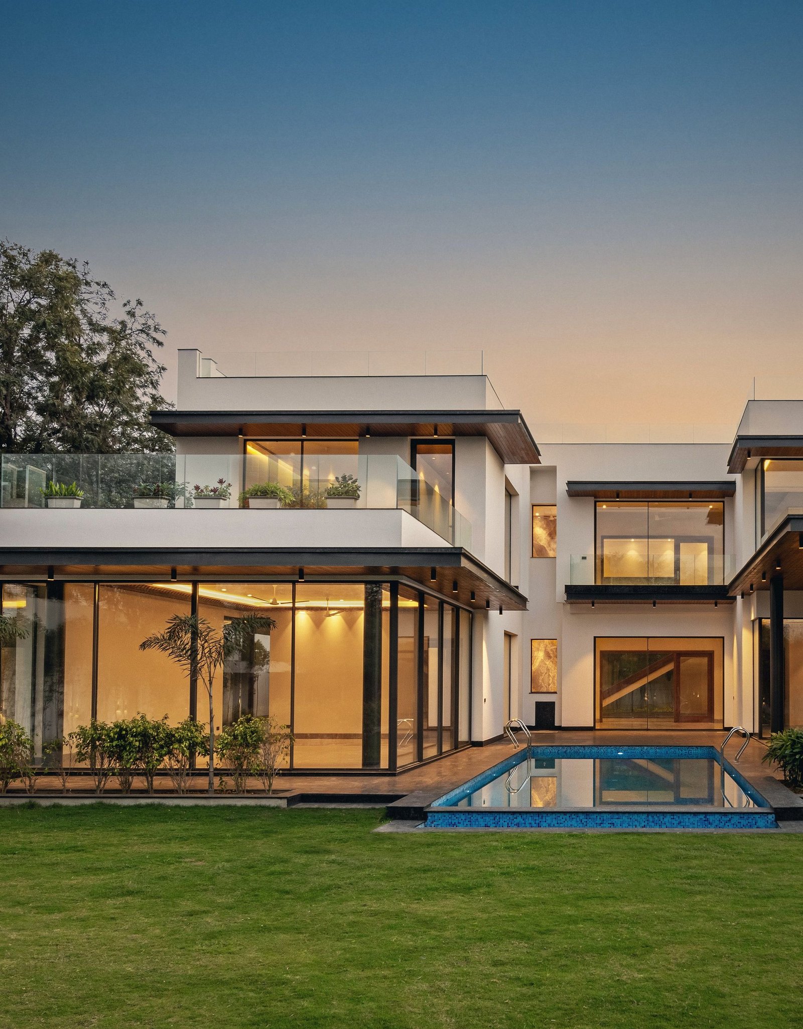 A BMB residence at dusk, its glass living rooms lit from within